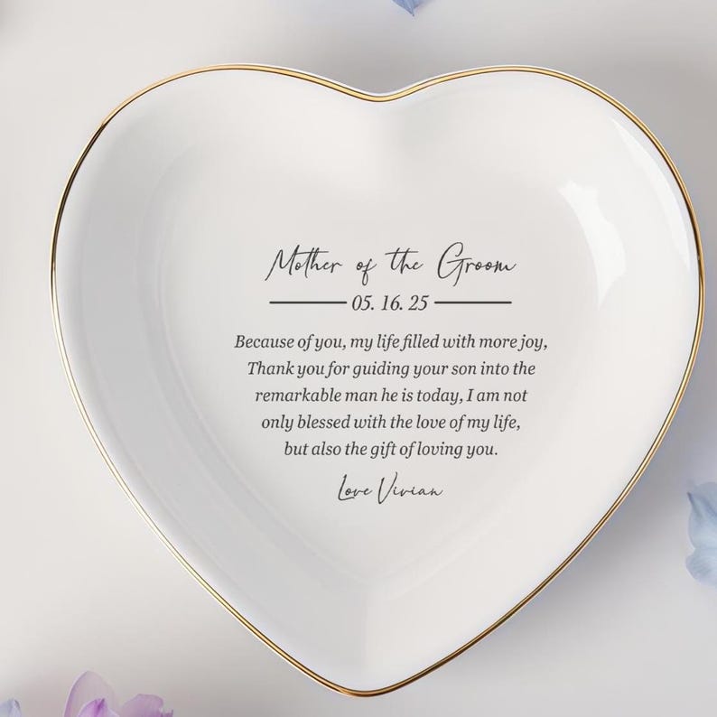 Op de afbeelding: Een hartvormige, witte keramische sieradenschaal met een gouden rand. De schaal heeft de tekst "Mother of the Groom" en een persoonlijke boodschap. Een attent cadeau voor een bruiloft.