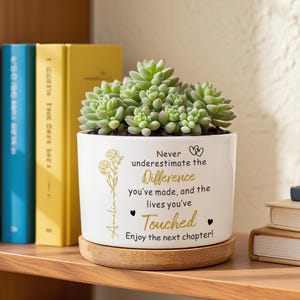 May include: A white ceramic plant pot with a succulent, on a wooden coaster. The pot has gold text: "Never underestimate the Difference you've made, and the lives you've Touched. Enjoy the next chapter!" A name is also printed.