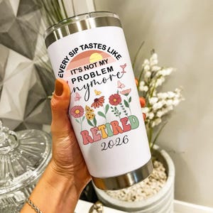 May include: A white stainless steel tumbler with a silver rim and base. The tumbler features the text "EVERY SIP TASTES LIKE IT'S NOT MY PROBLEM anymore" with a floral and butterfly design. The word "RETIRED" and the year "2026" are also displayed.