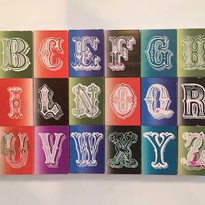 May include: A set of 26 alphabet blocks, each featuring a different letter in a decorative, vintage-style font. The blocks are arranged in alphabetical order and are painted in a variety of bright colors, including red, blue, green, and purple.