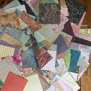 May include: A collection of patterned paper squares in various colors, including teal, pink, brown, and green. The papers feature different designs, such as floral, geometric, and abstract patterns.