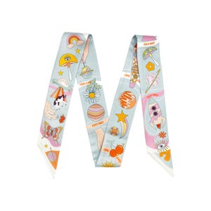 May include: A light blue silk scarf with a whimsical design featuring planets, mushrooms, rainbows, and the text "LUCY DALI". The scarf has a colorful, playful aesthetic with a variety of illustrations.