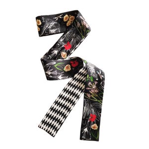 May include: A long, narrow black scarf featuring a white diamond pattern on one side and a detailed print of elephants, zebras, flowers, and dragonflies in white, red, and green on the other side. The fabric has a smooth, satin-like finish.