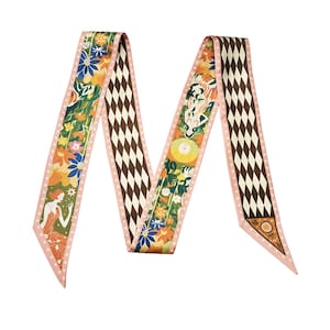 Könnte beinhalten: Langer, dekorativer Schal mit einem sich wiederholenden Muster aus braunen und weißen Rauten. Der Schal zeigt florale und Art-Déco-Illustrationen in Orange, Blau und Grün mit einem rosa Rand. Der Schal ist wahrscheinlich aus Seide oder einem ähnlichen leichten Material.