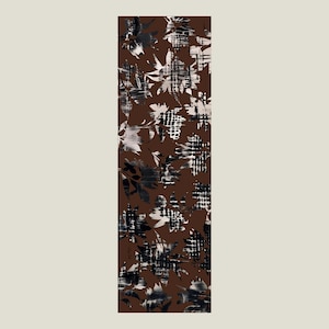 Peut inclure: Une écharpe rectangulaire avec un fond marron et un motif floral en noir, blanc et gris. Le motif présente des feuilles et des formes abstraites, créant un aspect texturé. Le motif de l'écharpe est répété sur toute sa longueur.