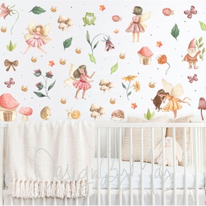 Puede incluir: Una cuna blanca con una manta rosa y blanca y un conejito de peluche blanco. La pared detr&aacute;s de la cuna est&aacute; decorada con una variedad de pegatinas de acuarela, incluyendo hadas, setas, flores y un gnomo.