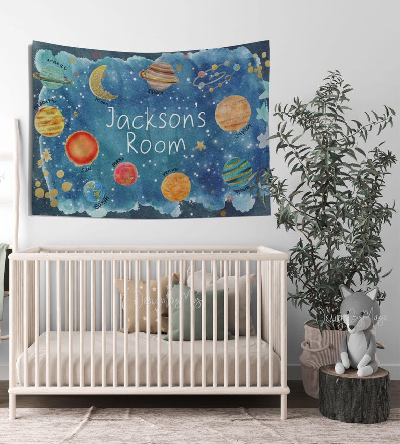 Pode incluir: Uma tape&ccedil;aria em estilo aquarela com uma cena espacial azul com planetas, estrelas e o texto "Jacksons Room". Os planetas s&atilde;o em v&aacute;rias cores, incluindo amarelo, laranja e azul. A tape&ccedil;aria est&aacute; pendurada acima de um ber&ccedil;o branco.