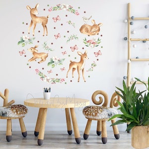 Puede incluir: Una pared blanca con una calcoman&iacute;a redonda de ciervos marrones y flores rosas. Dos taburetes de madera con forma de ciervo y una mesa de madera est&aacute;n frente a la pared. Una planta verde en una maceta de madera est&aacute; a la derecha de la imagen.
