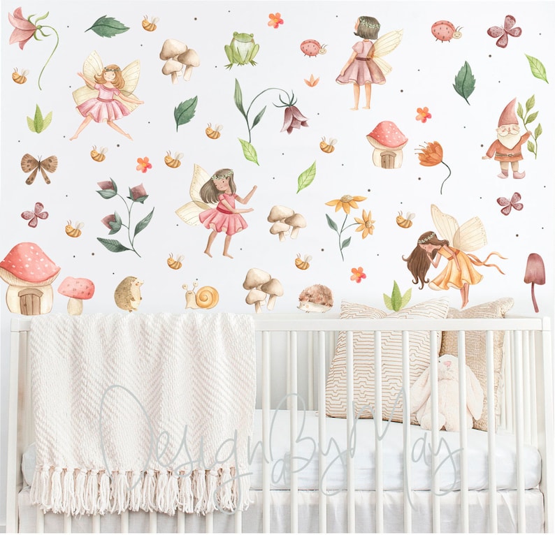 Puede incluir: Una cuna blanca con una manta rosa y blanca y un conejito de peluche blanco. La pared detr&aacute;s de la cuna est&aacute; decorada con una variedad de pegatinas de acuarela, incluyendo hadas, setas, flores y un gnomo.