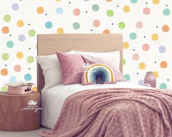 Puede incluir: Una escena de dormitorio con una cama cubierta con una manta y almohadas rosas. El cabecero es de madera clara. La pared tiene un patrón de lunares en colores pastel. También se ven una pequeña mesita de noche y un jarrón decorativo.