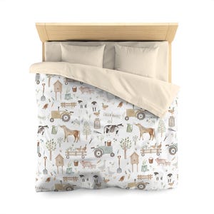 May include: A farmhouse-themed bedding set. The white duvet cover has a repeating pattern of farm animals, tractors, and gardening tools. The set includes two cream-coloured pillowcases and a cream-coloured duvet cover.