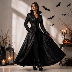May include: A long black leather coat with a high collar, long sleeves, and a single button closure at the waist. The coat features a fitted bodice that flares into a full-length skirt, paired with black trousers and black high-heeled boots.