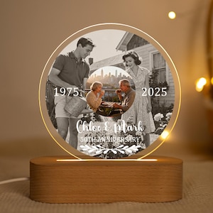以下が含まれることがあります： 木製の台座が付いた、パーソナライズされた記念日のフォトランプ。 ランプは、両側に「1975」と「2025」の文字、下に「50TH ANNIVERSARY」と「Chloe & Mark」の名前が書かれた、円形の照明付き写真が特徴です。