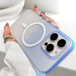 Pode incluir: Capa de telefone transparente com um anel magnético branco e uma borda azul. A capa tem um recorte para a câmera com três lentes pretas. Projetada para proteger o telefone e permitir o carregamento sem fio.