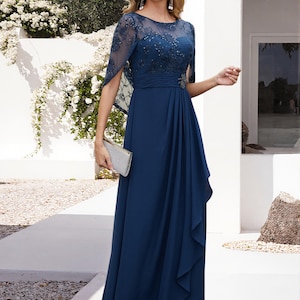 Op de afbeelding: Marineblauw avondjurk met een versierd lijfje en een zwierige rok. De jurk heeft een cape-achtig mouwdetail en wordt gecombineerd met een zilveren clutch. Geschikt voor speciale gelegenheden.