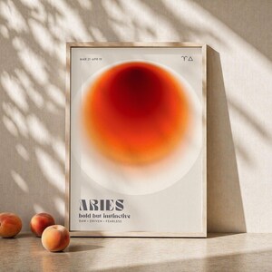 Könnte beinhalten: Ein gerahmter Kunstdruck mit einem abstrakten Design in Rot- und Orangetönen. Der Druck trägt die Aufschrift "ARIES" mit dem Text "bold but instinctive". Im Vordergrund liegen drei Pfirsiche.