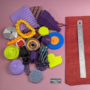 May include: A selection of brightly coloured 3D-printed objects in diverse shapes, such as a purple brick, a yellow heart, and a blue and orange circle. A red drawstring bag and a 15 cm ruler are also present.