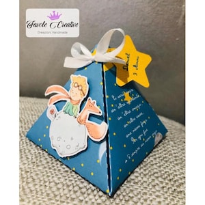 Può includere: Una scatola regalo blu a forma di piramide con pois bianchi, con un'illustrazione di un personaggio dei cartoni animati con una volpe. Un'etichetta gialla a forma di stella recita "Daniel 3 anni". La scatola ha un nastro bianco e il testo "Favole Creative".