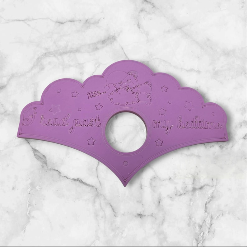 May include: A lilac-coloured bedtime story bookmark with a cloud and bear illustration. The text "I read past my bedtime" is featured, along with star accents and a circular opening.