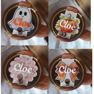 May include: Four tumbler lids with decorative toppers. One features a ghost, another a pumpkin, a third a floral design, and the last a bow. Each topper has the name "Cloe" in orange or white.