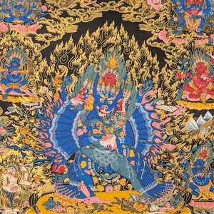 May include: A colorful Tibetan Buddhist Thangka painting depicting a deity with multiple arms and heads, surrounded by other figures and symbols. The painting is done in a traditional style with vibrant colors and intricate details.
