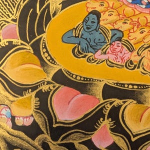May include: A detailed painting of a deity with a blue body and a yellow halo, surrounded by smaller figures. The deity is seated on a lotus flower with pink petals and a gold center. The background is black with gold accents.