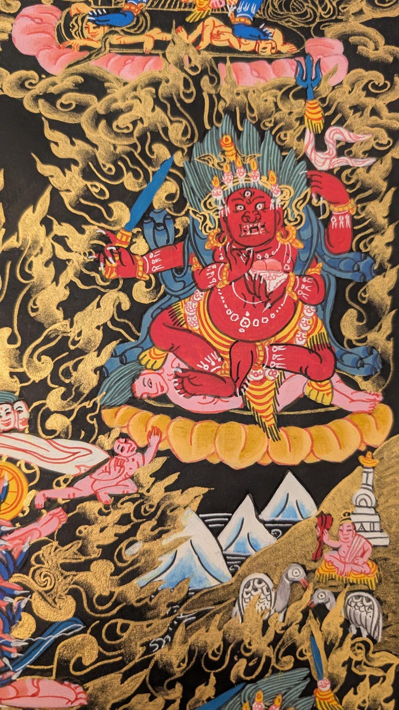 May include: A colorful Tibetan Buddhist painting depicting a deity with a red body, multiple arms, and a fierce expression. The deity is seated on a lotus throne surrounded by clouds and other figures. The painting is done in a traditional style with gold accents.