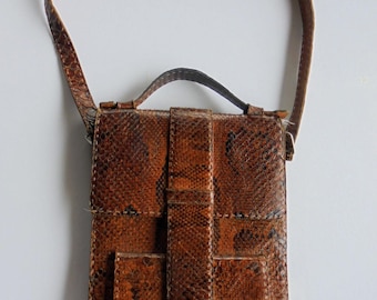 Peut inclure: Un sac vertical à motif peau de serpent marron doté d'une poignée supérieure et d'une longue bandoulière. Le sac présente une sangle verticale centrale qui se ferme avec un fermoir en métal argenté et une petite poche avant à rabat.