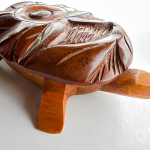 Può includere: Statuetta di tartaruga in legno intagliato a mano. La tartaruga ha un guscio marrone scuro con intagli dettagliati e zampe e testa marrone chiaro. Il guscio presenta motivi di foglie e fiori. Oggetto decorativo.