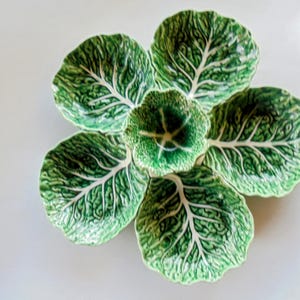 Puede incluir: Un juego de seis platos de cerámica dispuestos en forma de flor. Los platos son verdes con vetas blancas, que se asemejan a hojas de col. El plato central es más pequeño y redondeado. Ideal para servir aperitivos o porciones pequeñas.