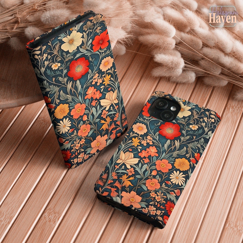 May include: Two phone cases with a floral pattern. The cases have a dark teal background with red, orange, and yellow flowers and green leaves. The cases are on a wooden surface.