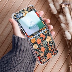 May include: A floral patterned phone case with a dark background and orange, yellow, and red flowers. The phone case is open, revealing the phone screen displaying the date and time. The case is clear around the edges.