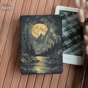 May include: A Kindle cover featuring a landscape illustration with a full moon, mountains, and a river. The cover is dark with a detailed design. The word "Haven" is in the upper left corner. A white Kindle is next to the cover.