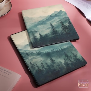 May include: Two square e-reader cases featuring a printed landscape illustration of a misty forest with tall pine trees and distant mountains in shades of teal, green, and cream. The cases are stacked, displaying a consistent nature-themed design.