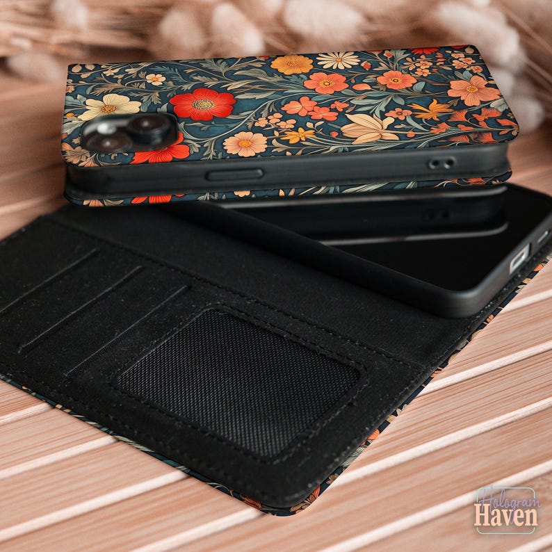 May include: A floral patterned phone case with a wallet design. The case has a dark blue background with red, orange, and yellow flowers. The wallet section is black and includes card slots and a clear ID window. The phone is black.