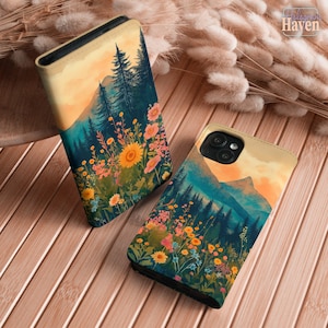 Pode incluir: Duas capas de telemóvel com um design de paisagem impresso de uma cordilheira, pinheiros verde-escuros e um campo de flores silvestres coloridas sob um céu de pôr do sol em tons suaves de laranja e amarelo. As capas têm acabamento liso.