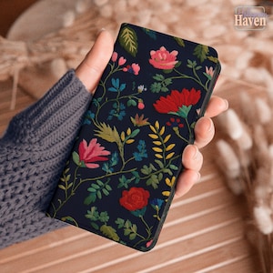 May include: A rectangular phone case featuring a dark navy blue background with an intricate embroidered floral pattern. The design includes various flowers in shades of red, pink, and yellow, accompanied by green leaves and thin stems.