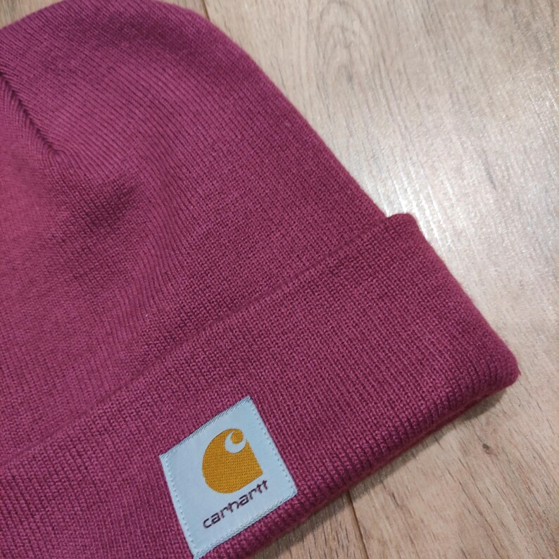 Puede incluir: Un gorro de punto burdeos con borde doblado. Una etiqueta cuadrada con el logotipo de Carhartt est&aacute; cosida en la parte delantera. El gorro est&aacute; hecho de tejido de punto acanalado.