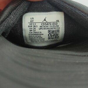 May include: Close-up of a black shoe label with white text. The label includes size information: US 6Y, UK 5.5, EUR 38.5, cm 24, and BR 37. The label also displays a product code, manufacturing details, and a QR code.