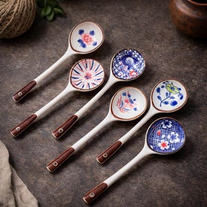 May include: Six ceramic spoons with white handles and brown wooden grips. Each spoon bowl features a unique floral design in shades of blue, pink, and yellow. The spoons are arranged on a dark, textured surface.