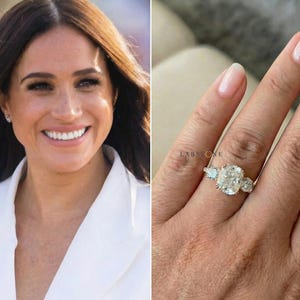 Può includere: Un anello di fidanzamento in oro con un grande diamante centrale a taglio cuscino e due pietre laterali più piccole. L'immagine mostra anche una donna sorridente.