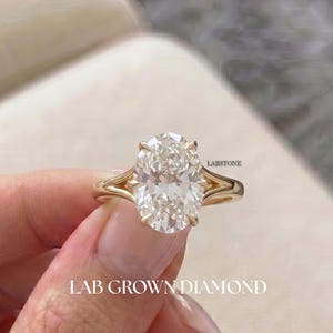 Könnte beinhalten: Ein goldener Ring mit einem großen, oval geschliffenen Labor-Diamanten. Der Ring hat ein geteiltes Schaftdesign. Der Text "LAB GROWN DIAMOND" ist unten im Bild zu sehen.