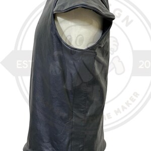 May include: A black leather vest with a unique design. The vest has a rounded shoulder cut and a smooth, matte finish. The garment is displayed on a mannequin, showcasing its shape and texture. The vest appears to be a sleeveless top.