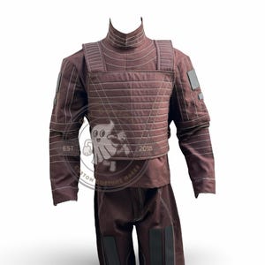 May include: A brown costume with a high collar, quilted chest piece, and long sleeves. The costume includes matching trousers with black accents. The words "EST" and "2018" are visible on the image.