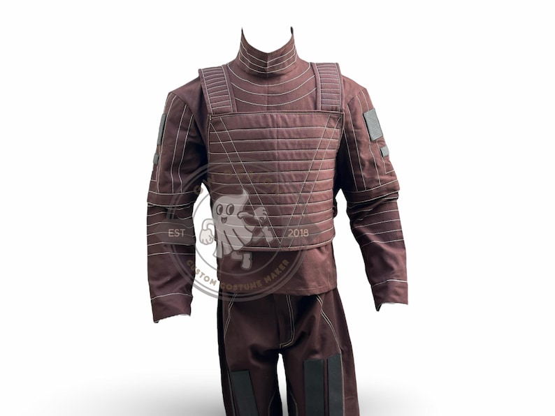 May include: A brown costume with a high collar, quilted chest piece, and long sleeves. The costume includes matching trousers with black accents. The words "EST" and "2018" are visible on the image.