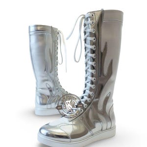 Puede incluir: Botas plateadas hasta la rodilla con cordones blancos y un diseño de llamas. Las botas tienen una suela blanca y un acabado metálico brillante. Diseño de vestuario personalizado.