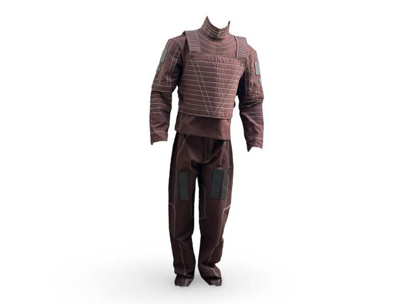 May include: A brown tactical suit, comprising a high-collared top, quilted vest, and matching trousers. The suit has reinforced patches on the shoulders, elbows, and knees. The stitching is a lighter brown, creating a contrast against the darker fabric.