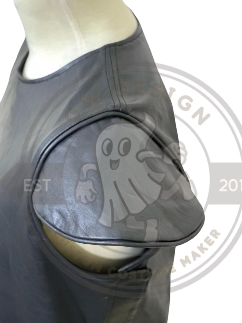 May include: Close-up of a gray, sleeveless top with a unique cut-out design on the shoulder. The top is made of a smooth, possibly leather-like material. The design includes a ghost-like logo.