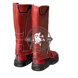 Peut inclure: Une paire de bottes de costume rouges et noires. Les bottes montent jusqu'aux genoux avec une tige rouge textur&eacute;e et des accents noirs. Les semelles sont noires. Les bottes ont un design qui comprend une sangle et une boucle. Fabriqu&eacute; par un fabricant de costumes.