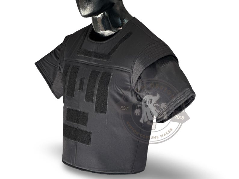 May include: Black tactical vest with short sleeves, featuring multiple rectangular velcro patches on the front. The vest is displayed on a mannequin. The image includes a logo with the text "CUSTOM COSTUME MAKER EST 2018".